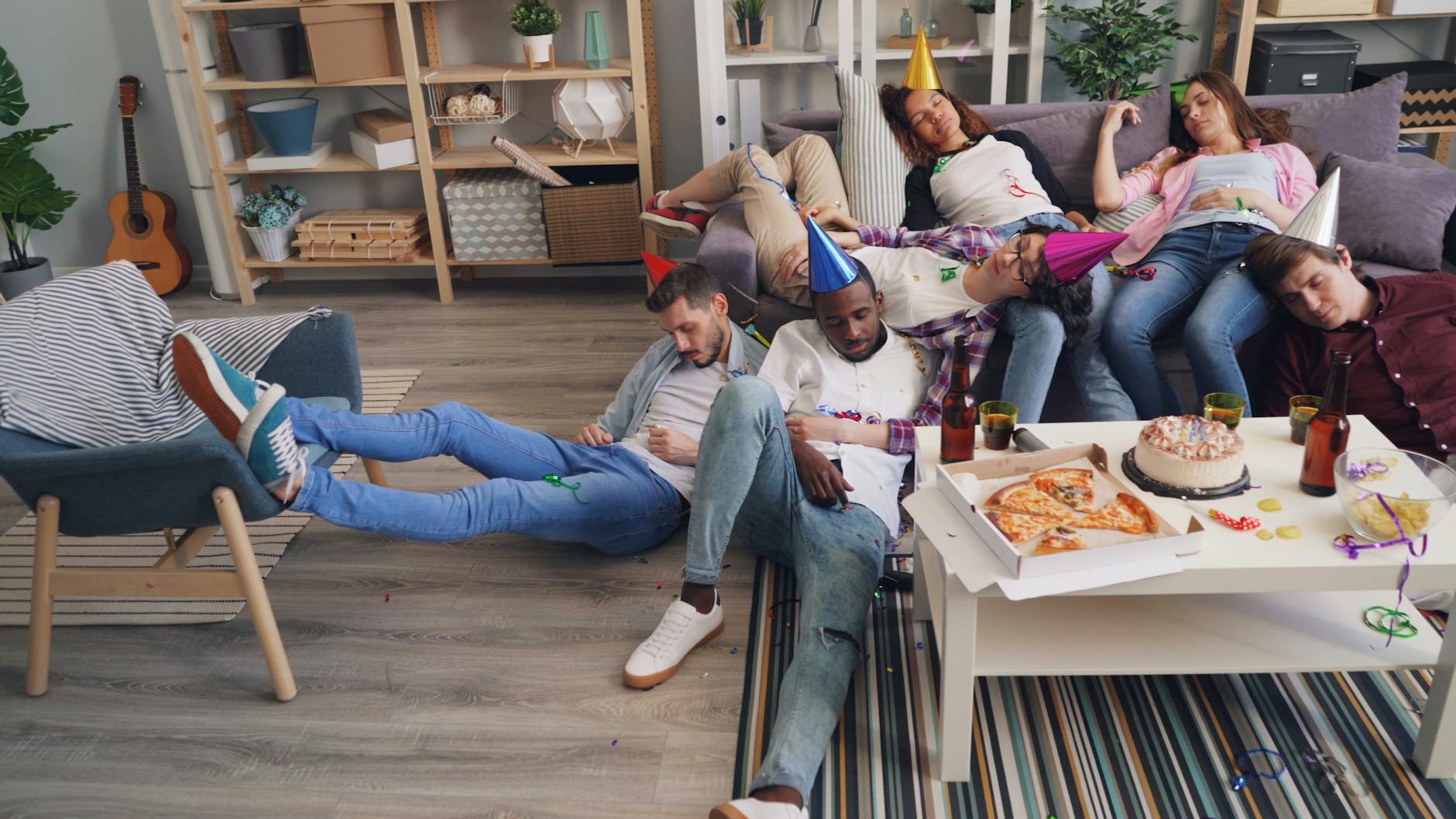 Znajomi śpią zmęczeni po domówce, wokół widać jedzenie i dekoracje