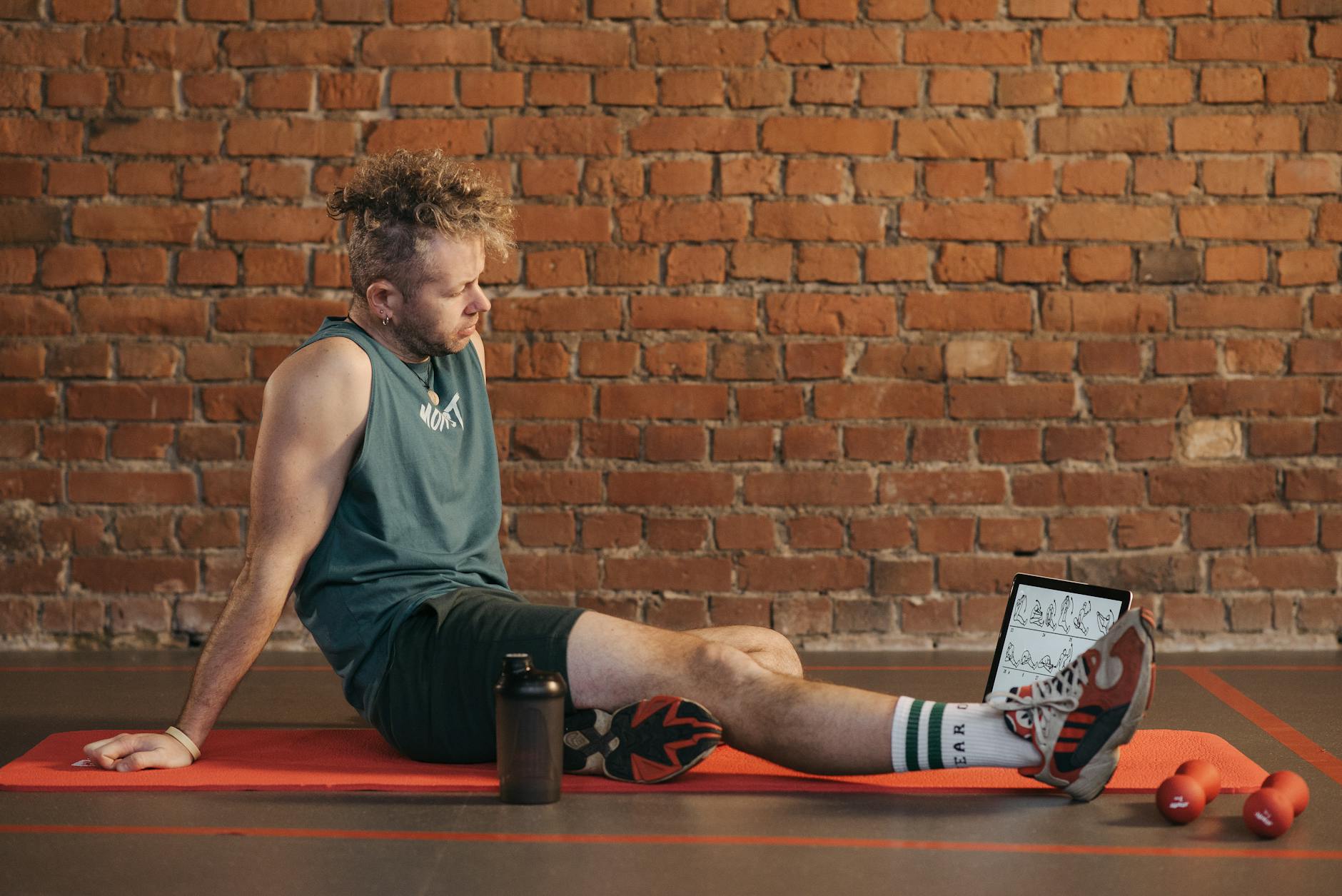 Sportowiec odpoczywa na macie w siłowni miejskiej obok ciężarów i tabletu