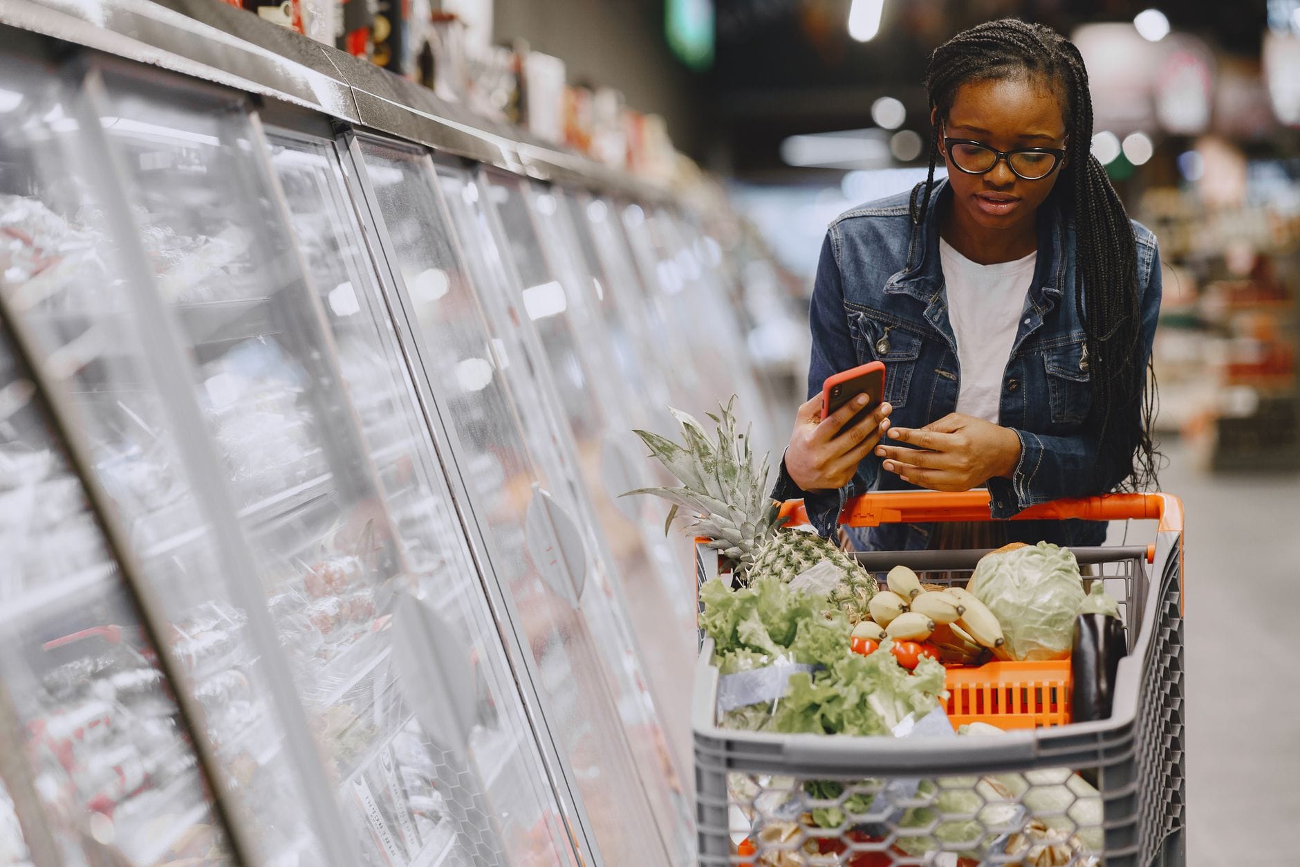 Kobieta z telefonem przy wózku pełnym zakupów w supermarkecie