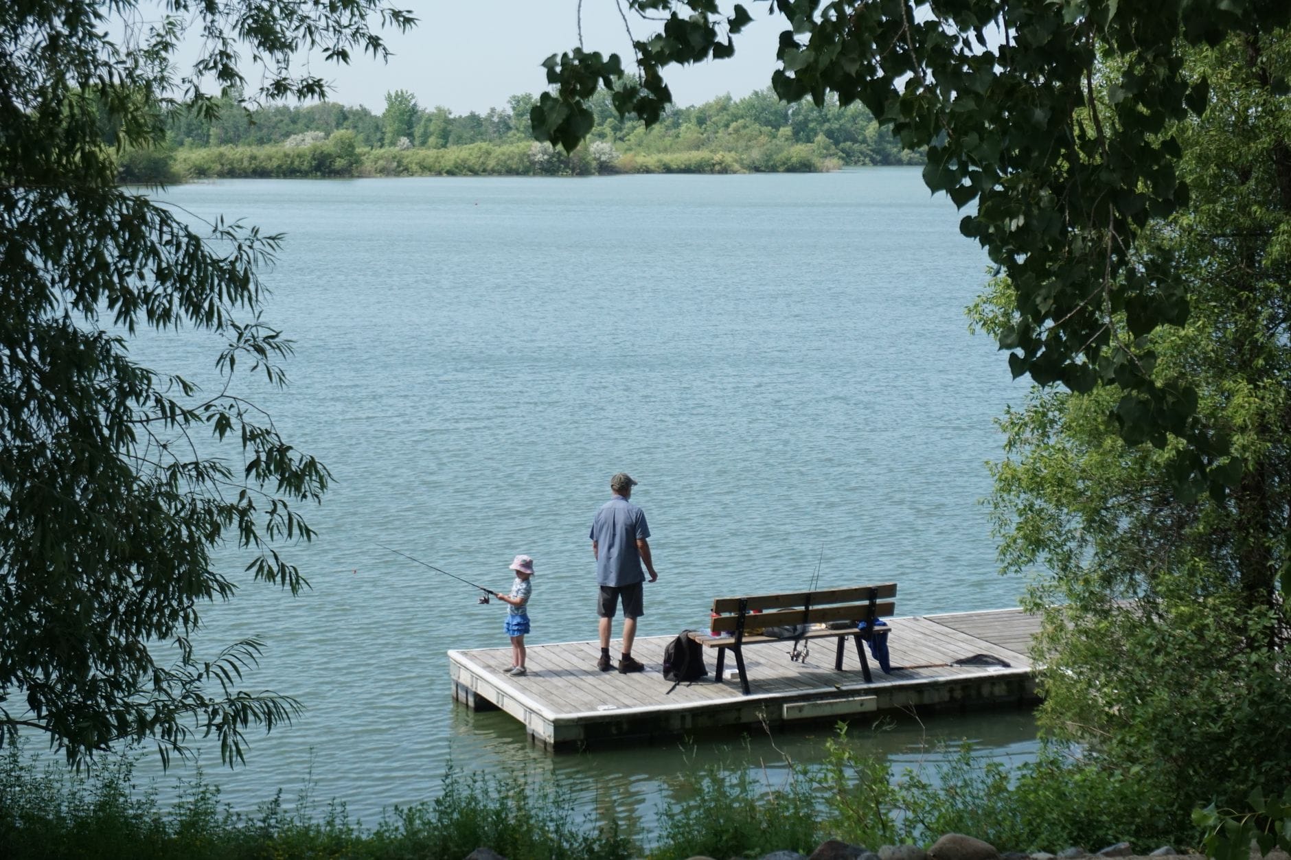 Ojciec i córka wędkują razem na pomoście nad spokojnym jeziorem