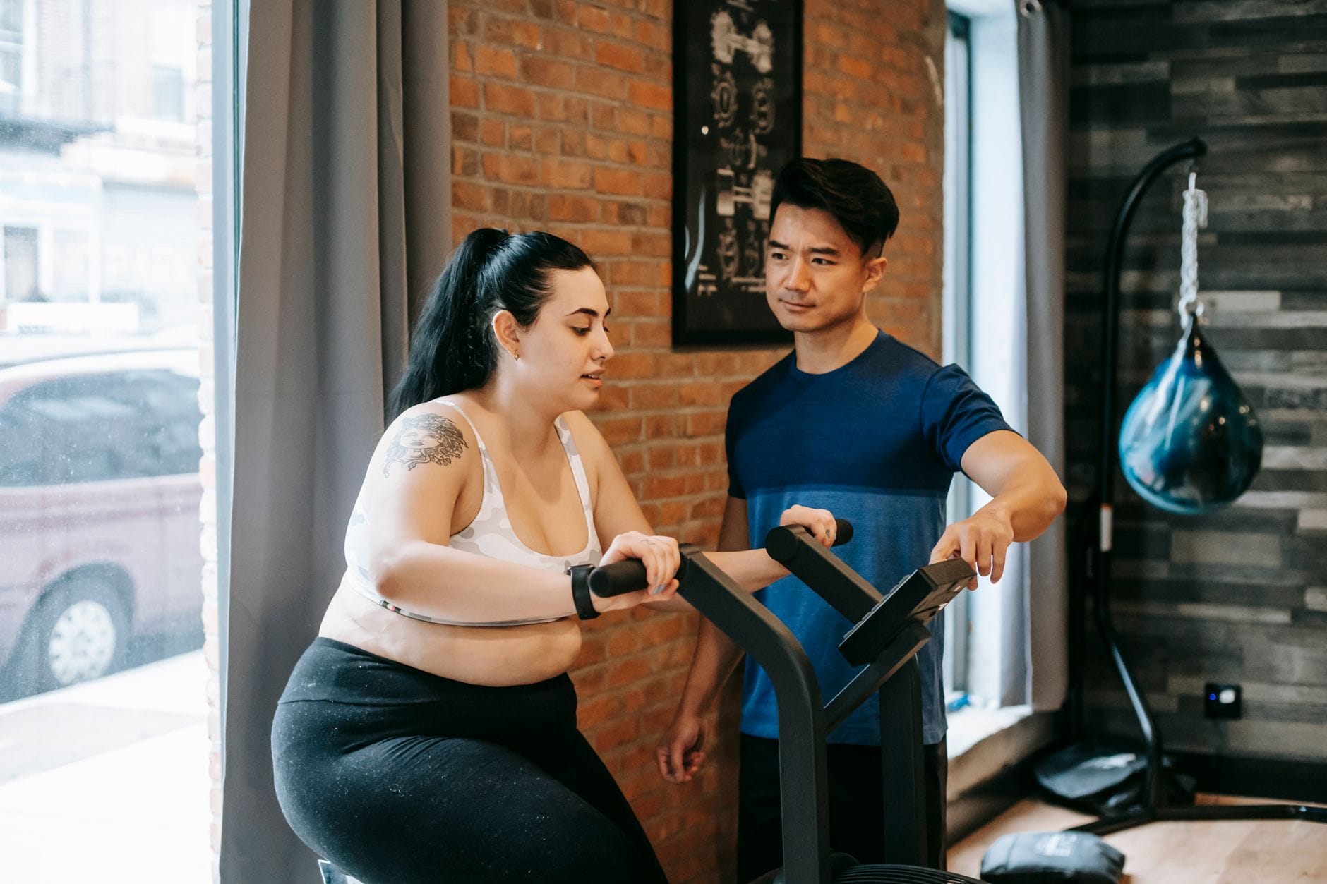 Trener personalny pomaga kobiecie plus size ćwiczyć na rowerku w siłowni